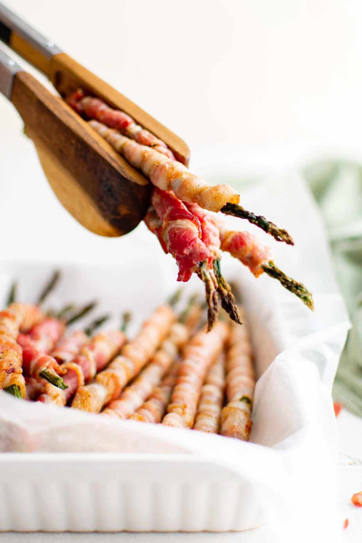 Wooden tongs holden a few pieces of asparagus wrapped in bacon.