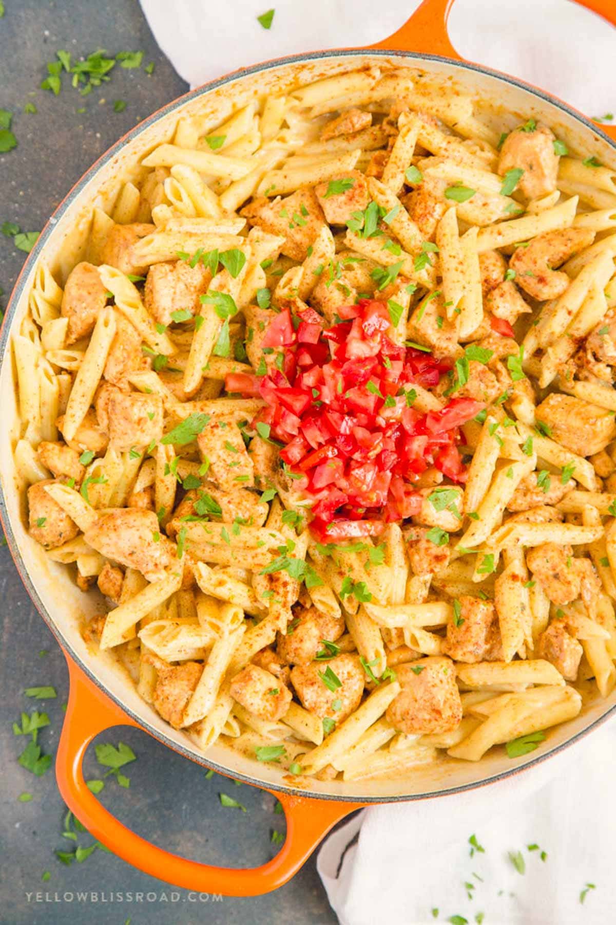 Pasta and chicken with diced tomatoes in a creamy sauce and in a large skillet with orange handles.