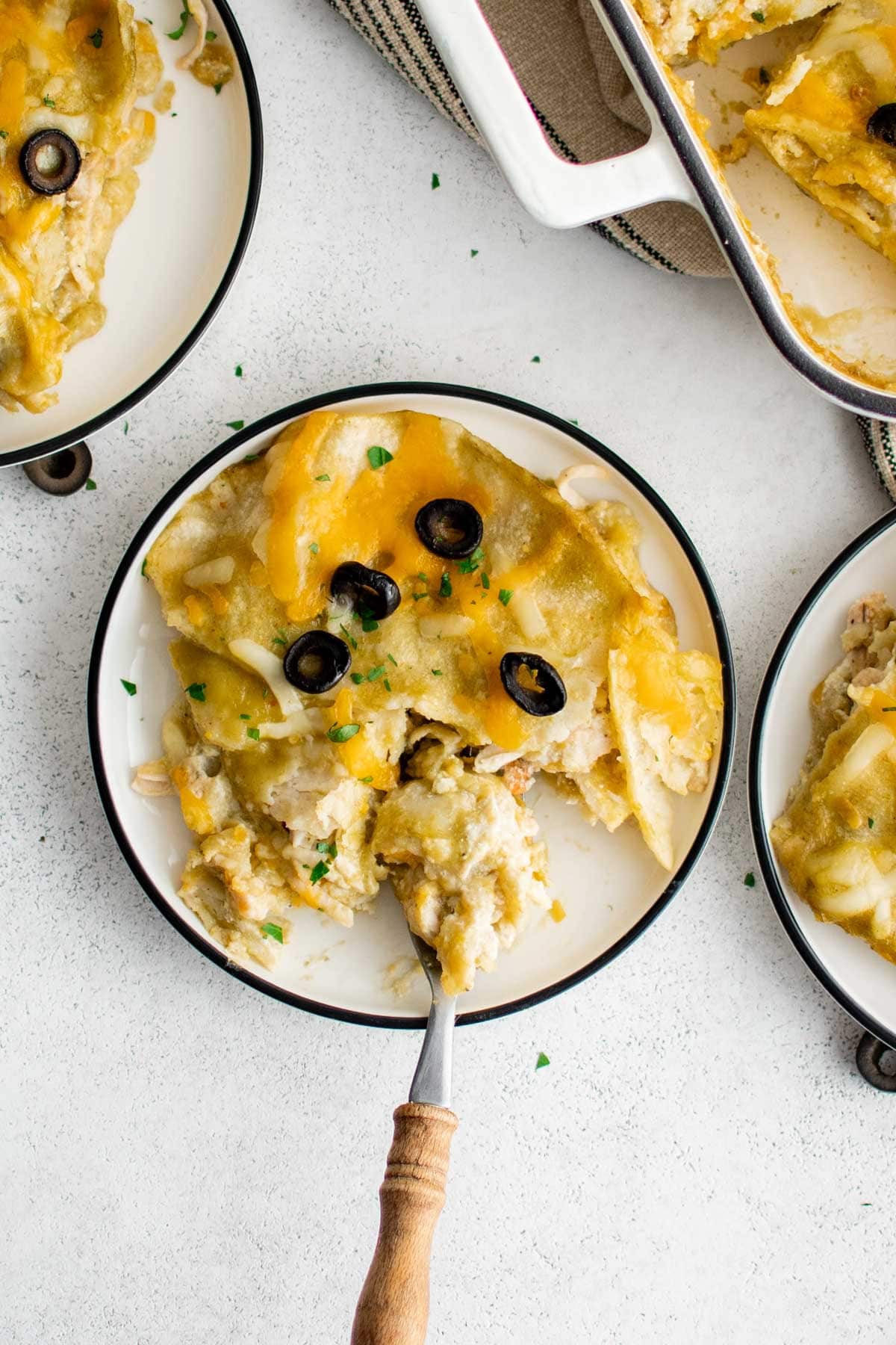 Slice of chicken enchilada casserole on a small white plate with a black rim, and with a fork.