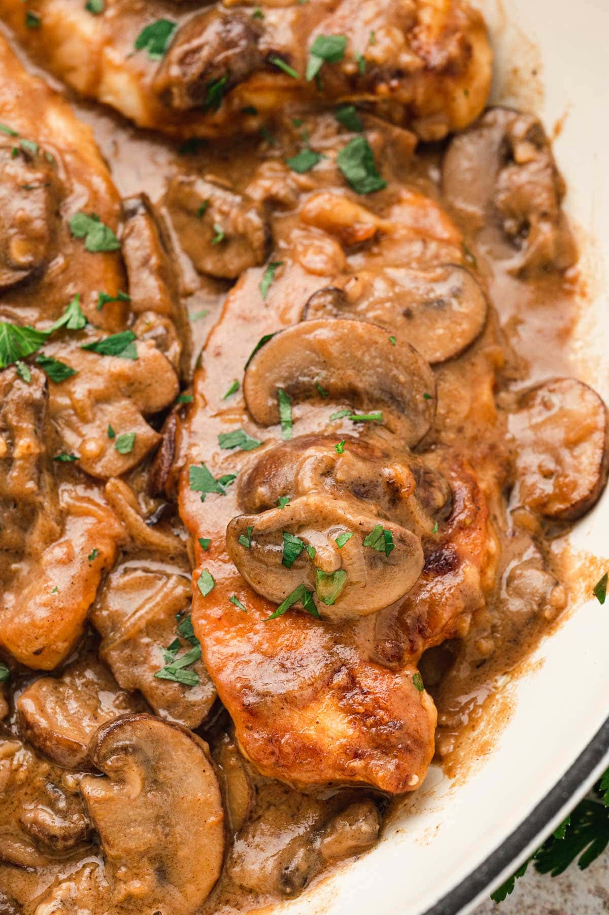 Piece of chicken breast in a brown sauce with mushrooms.
