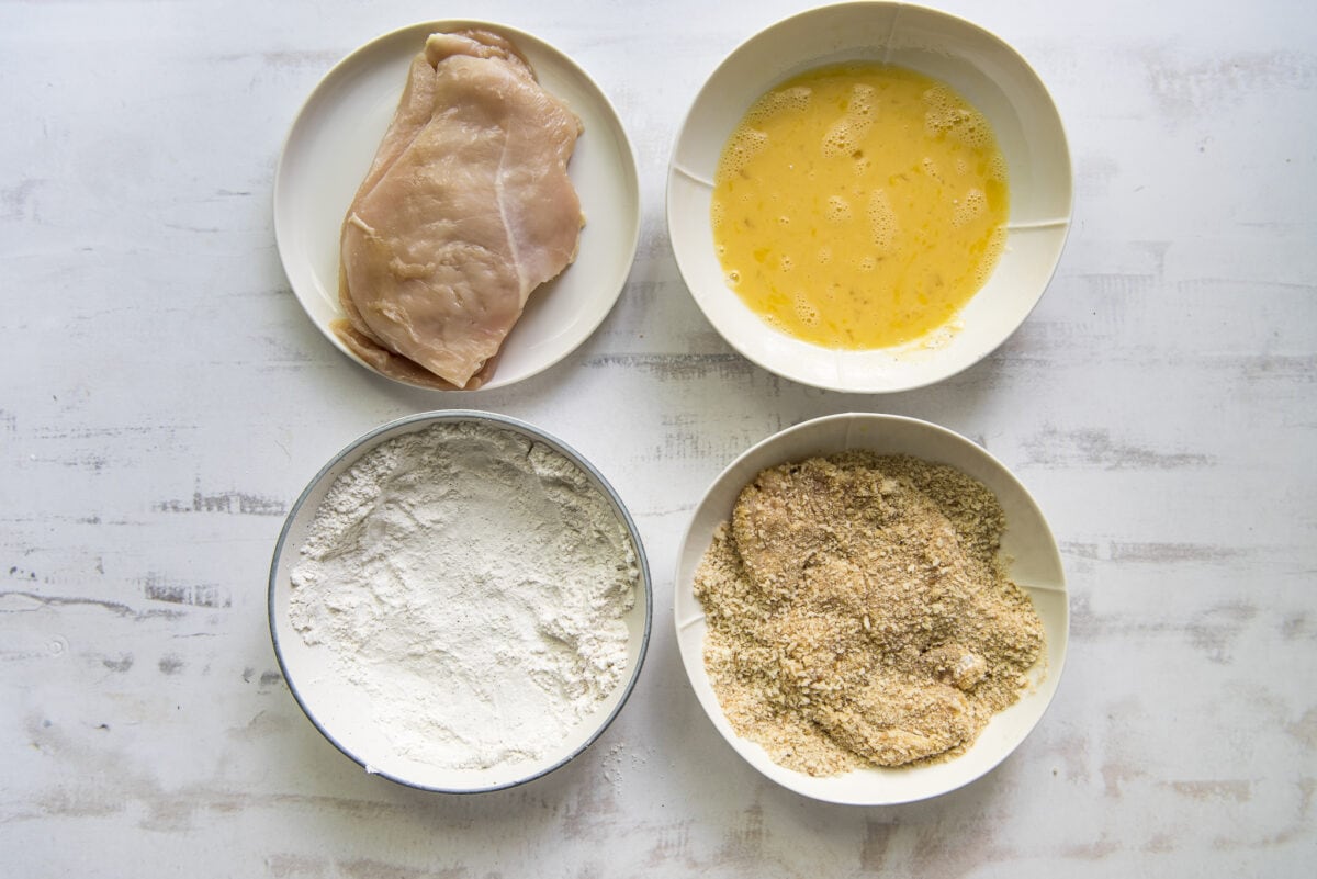 Chicken breading station with chicken piece in the breadcrumbs.