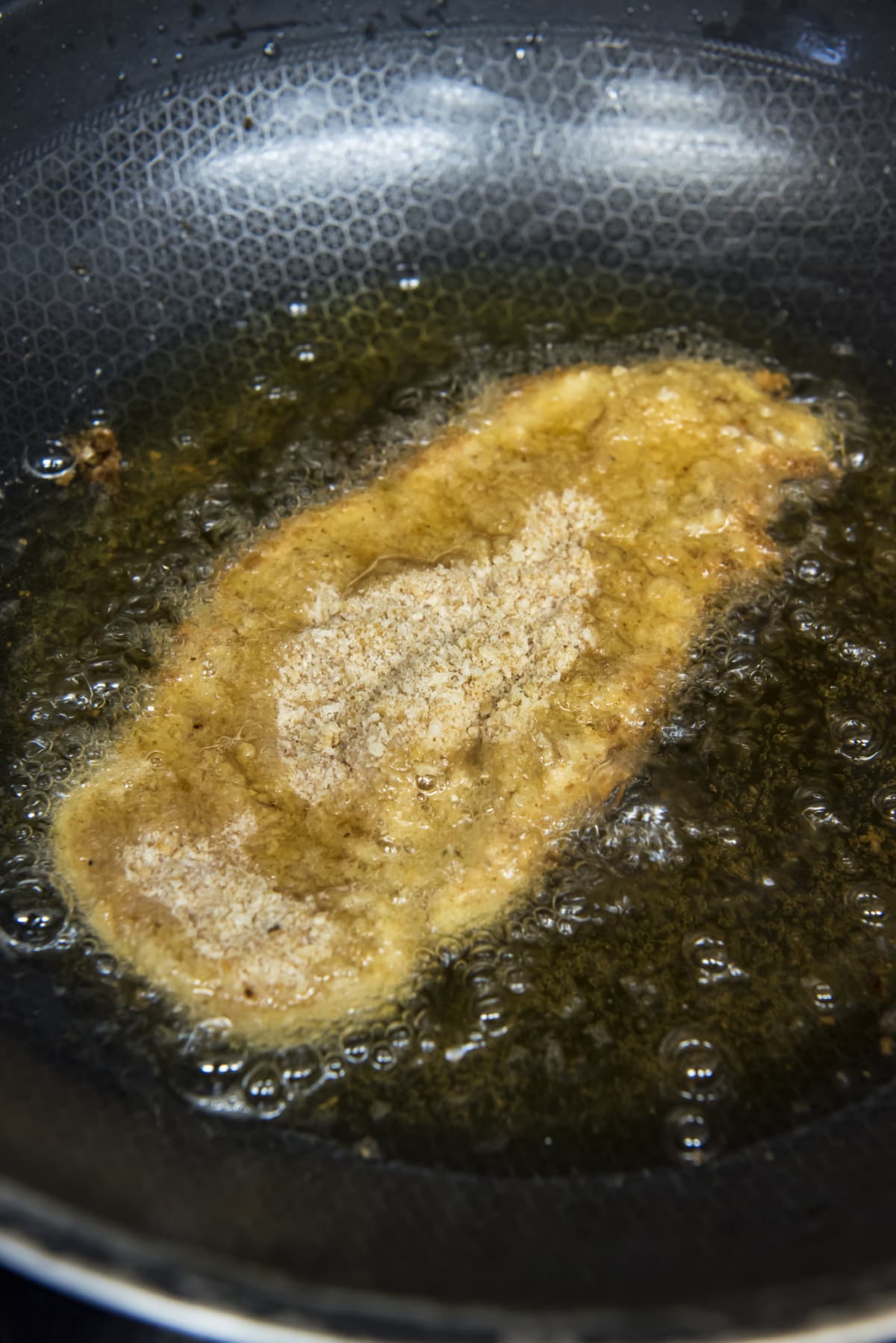 Breaded chicken breast frying in oil in a cast iron skillet.