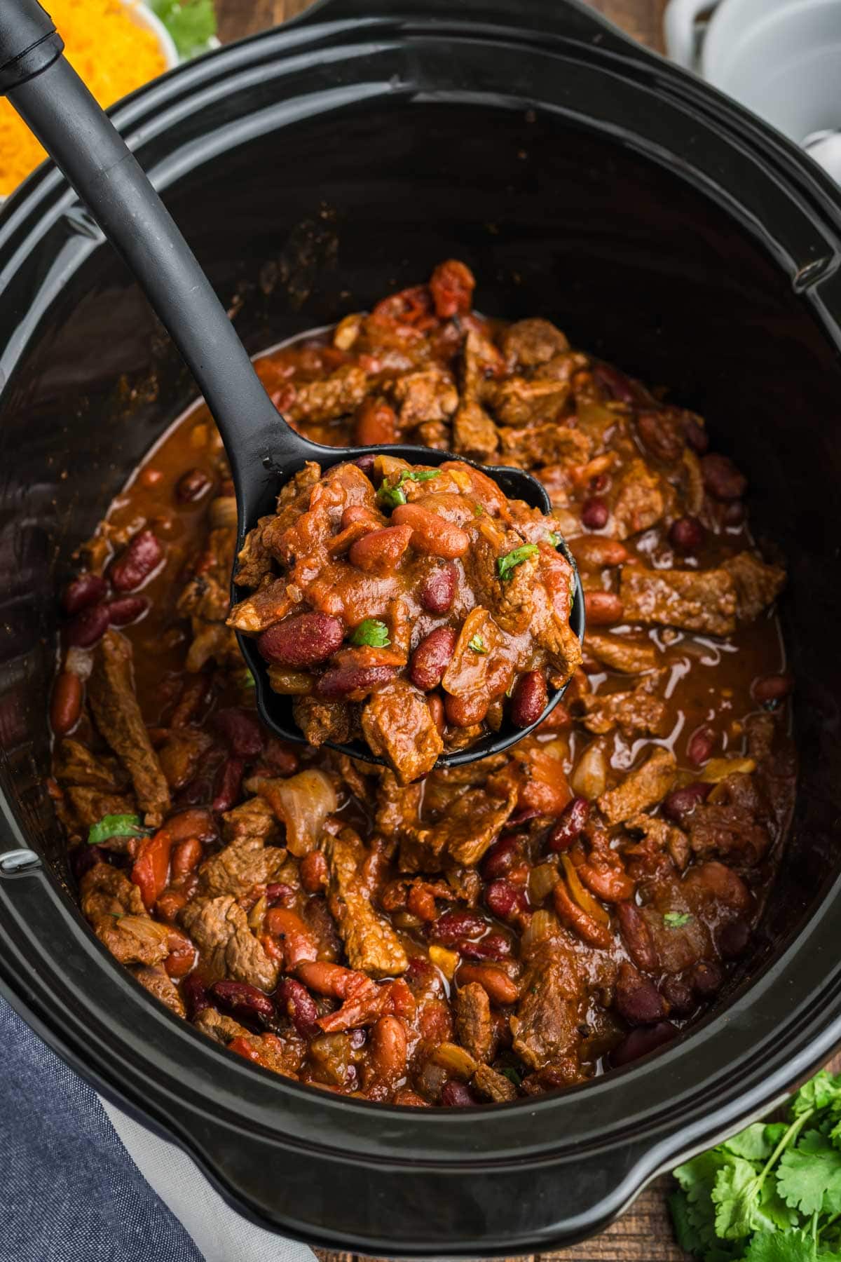 Steak chili in a slow cooker with a ladle.