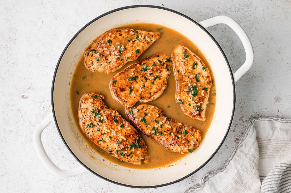 Chicken breasts with garlic and parsley in a light brown butter sauce in a cream colored skillet.