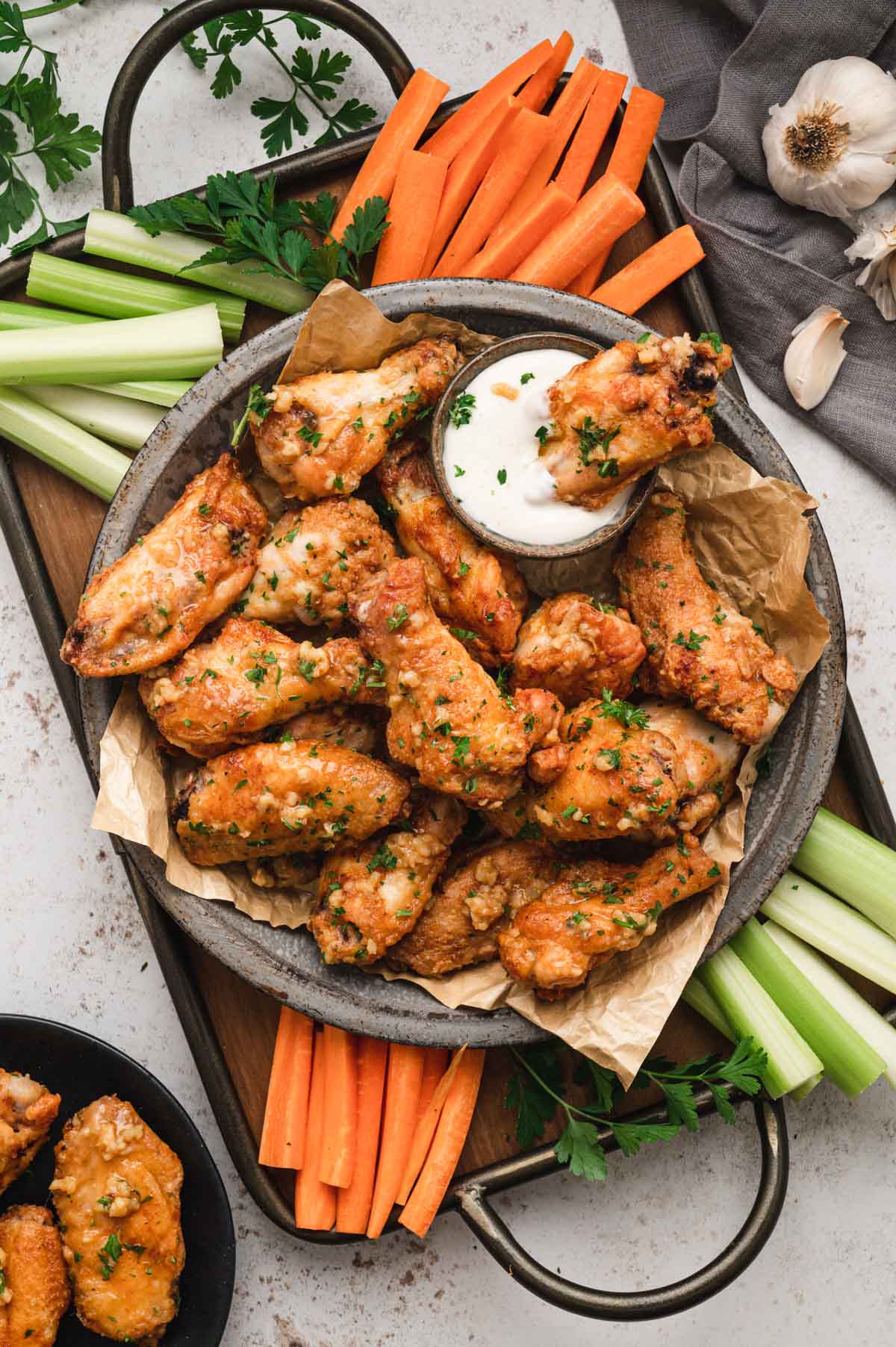 Chicken wings, on a silver tray with large handles, surrounded by celery and carrot sticks.
