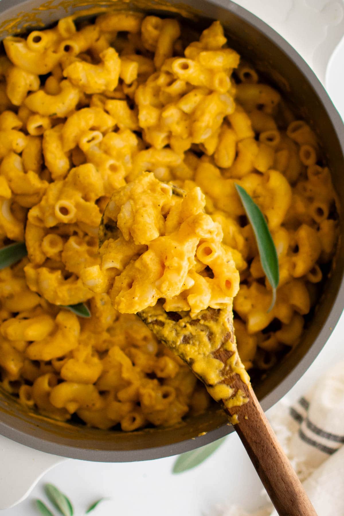 Wooden spoon with pumpkin mac and cheese over a saucepan.