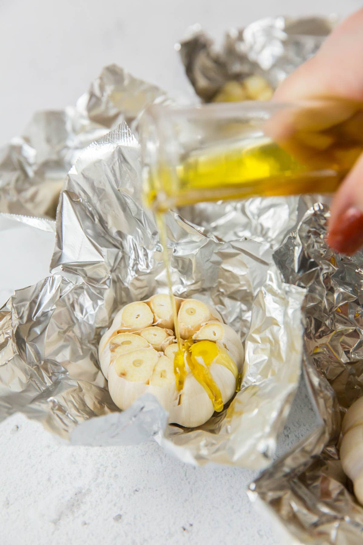 Head of raw garlic drizzled with olive oil and sitting on a piece of foiil.