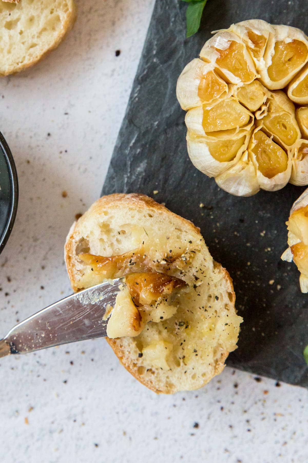 Mashed roasted garlic spread onto a slice of baguette with black pepper.