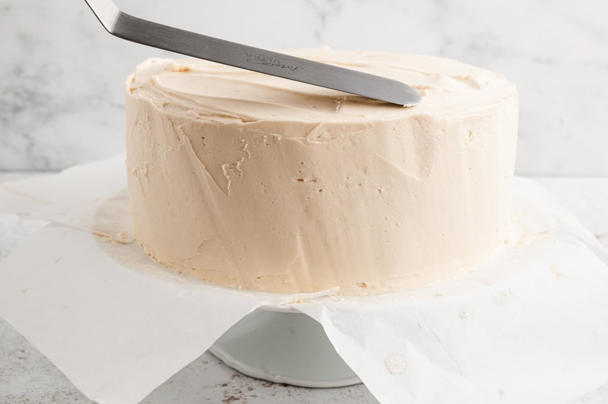 Using a flat spatula to spread frosting on a round layer cake.