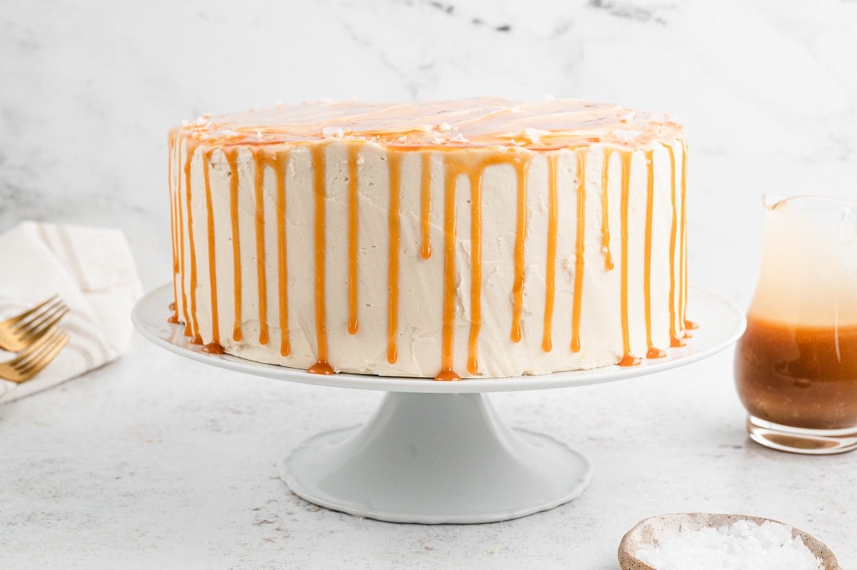 A layer cake with light tan caramel icing and caramel sauce dripping down the sides.