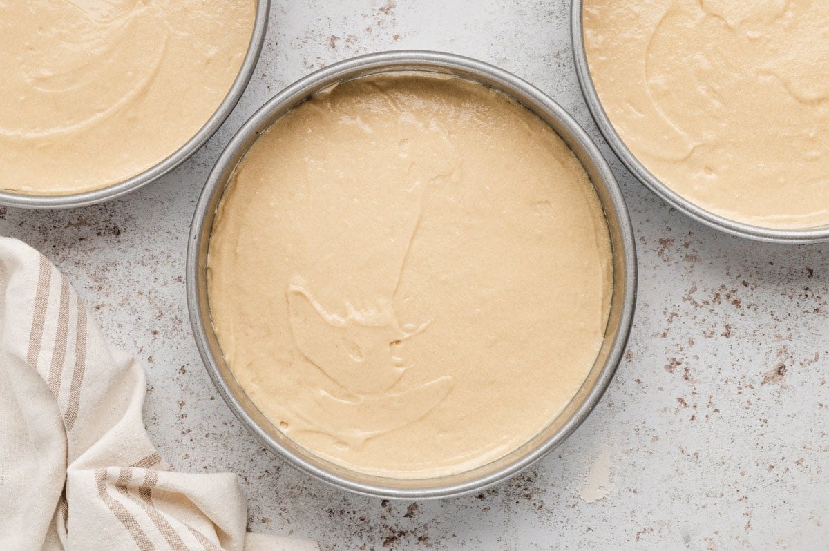 Three round cake pans filled with batter.