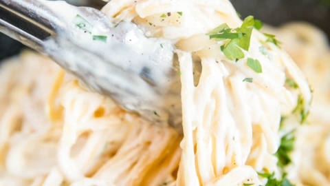 Fettuccine Alfredo being tossed with metal tongs in a saute pan.