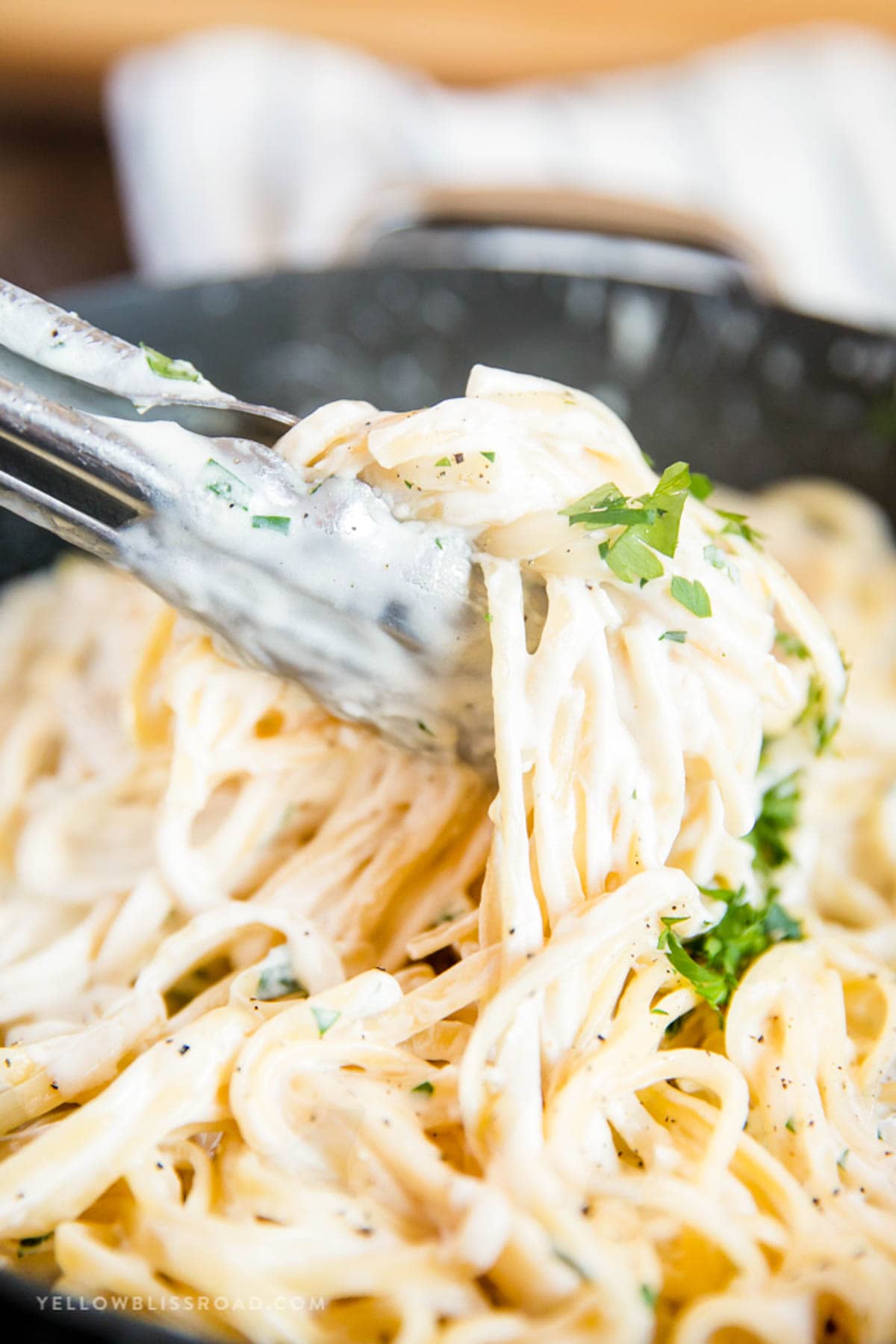 Fettuccine Alfredo being tossed with metal tongs in a saute pan.