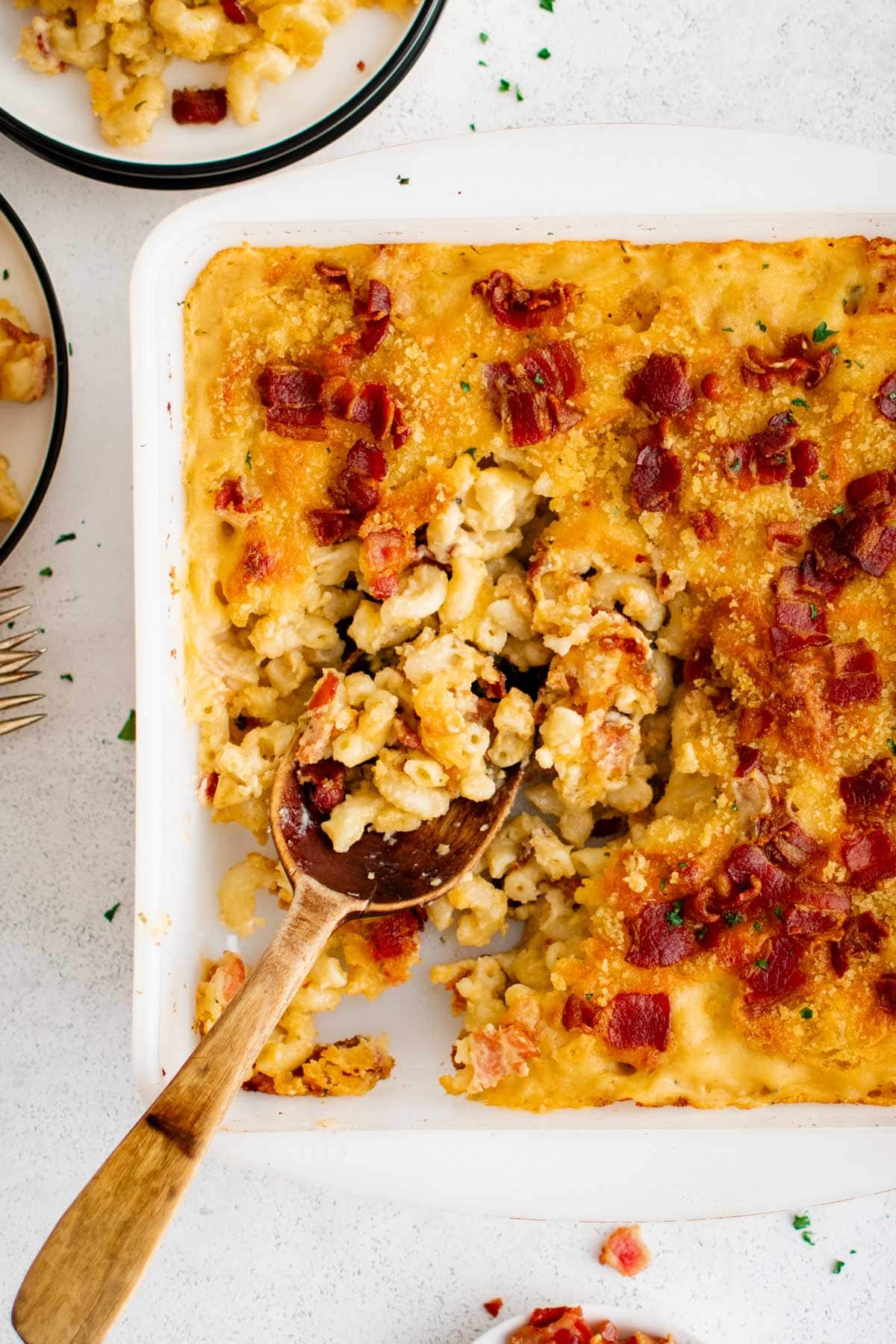 Bacon mac and cheese in a square baking dish with a gold serving spoon.