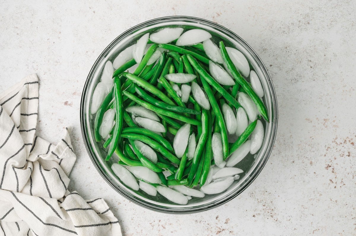 Green beans and ice water in a large glass bowl.