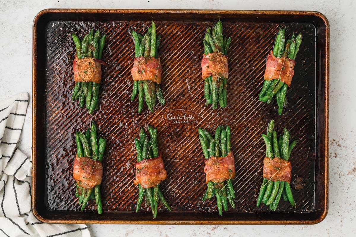 Cooked green beans wrapped in bacon on a sheet pan.