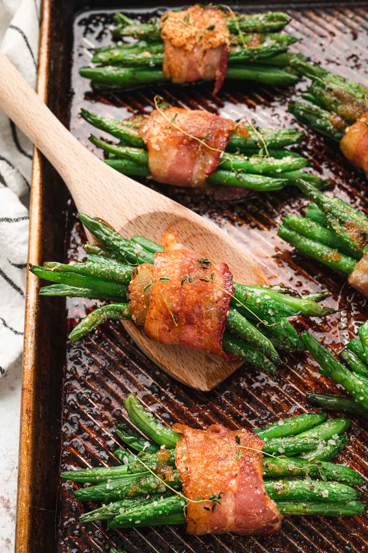 Bacon wrapped green beans on a sheet pan with a wooden spoon.