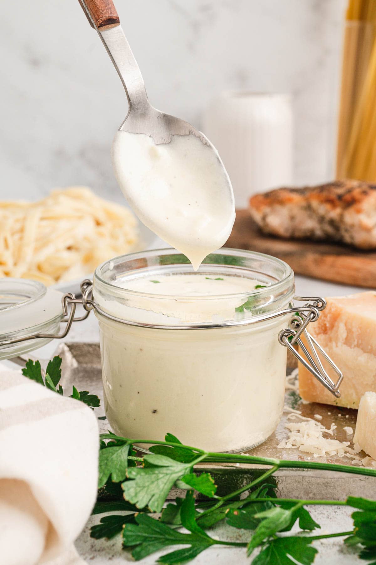Glass jar filled with alfredo sauce, a spoon dripping sauce above the jar.