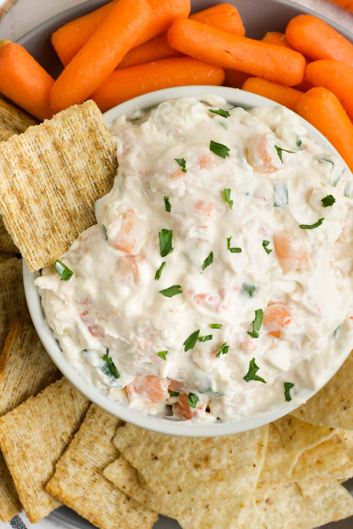 Creamy shrimp dip in a small dish surrounded by baby carrots and Triscuit crackers.