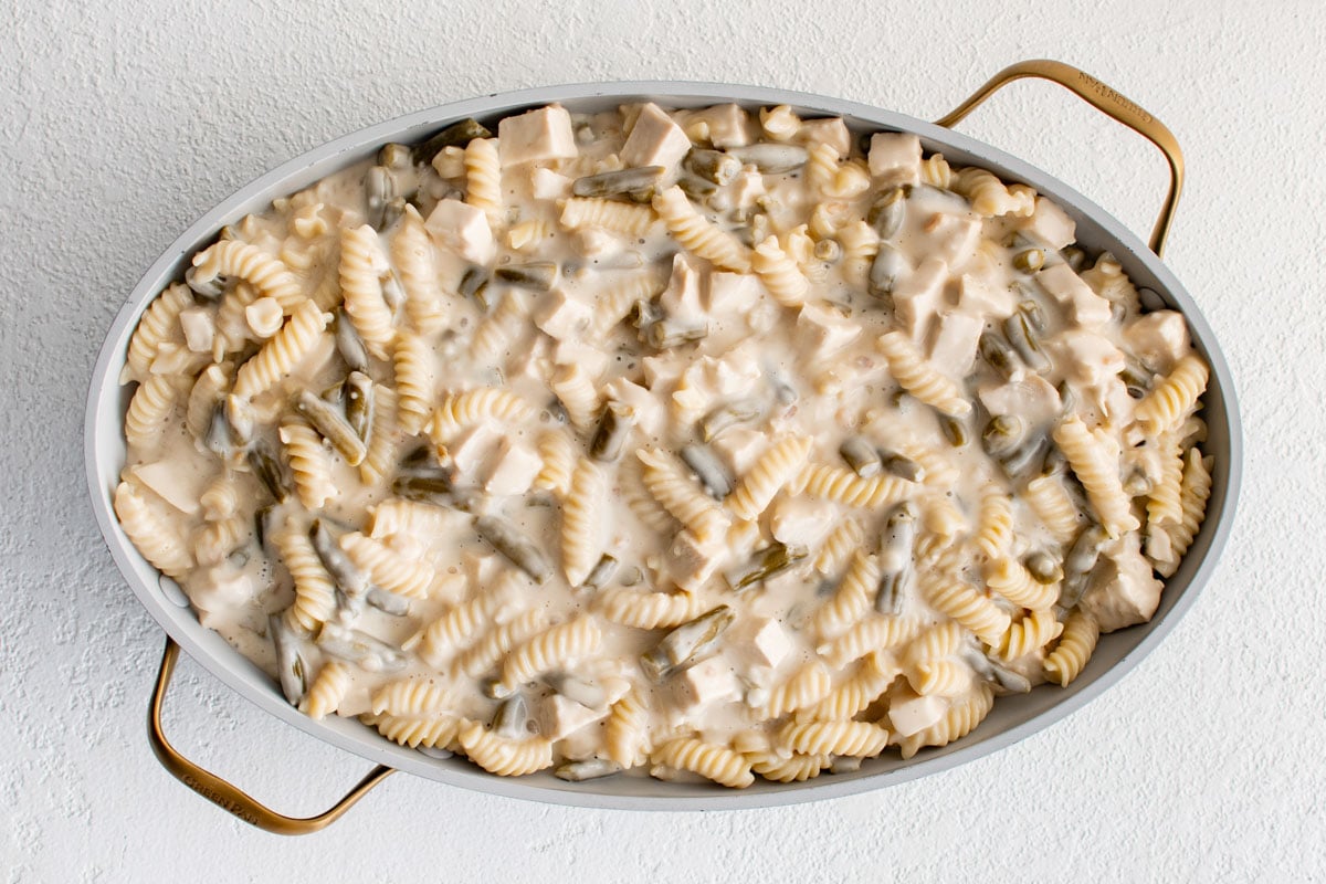 Creamy sauce over chicken green beans and boodles in a baking dish.