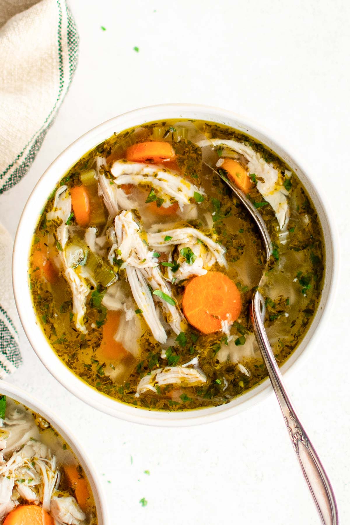 Chicken, carrots and herbs in soup broth in a small bowl with a spoon