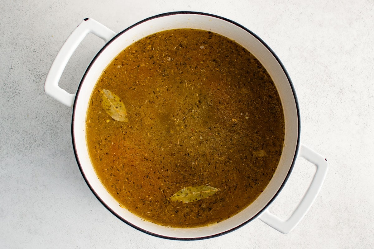 Broth in a soup pot, with herbs floating.