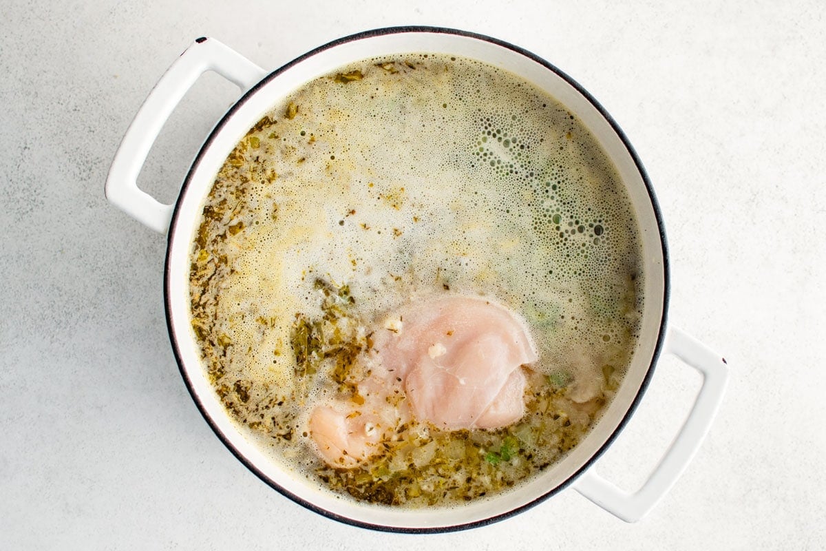 Raw chicken pieces in chicken broth with herbs.