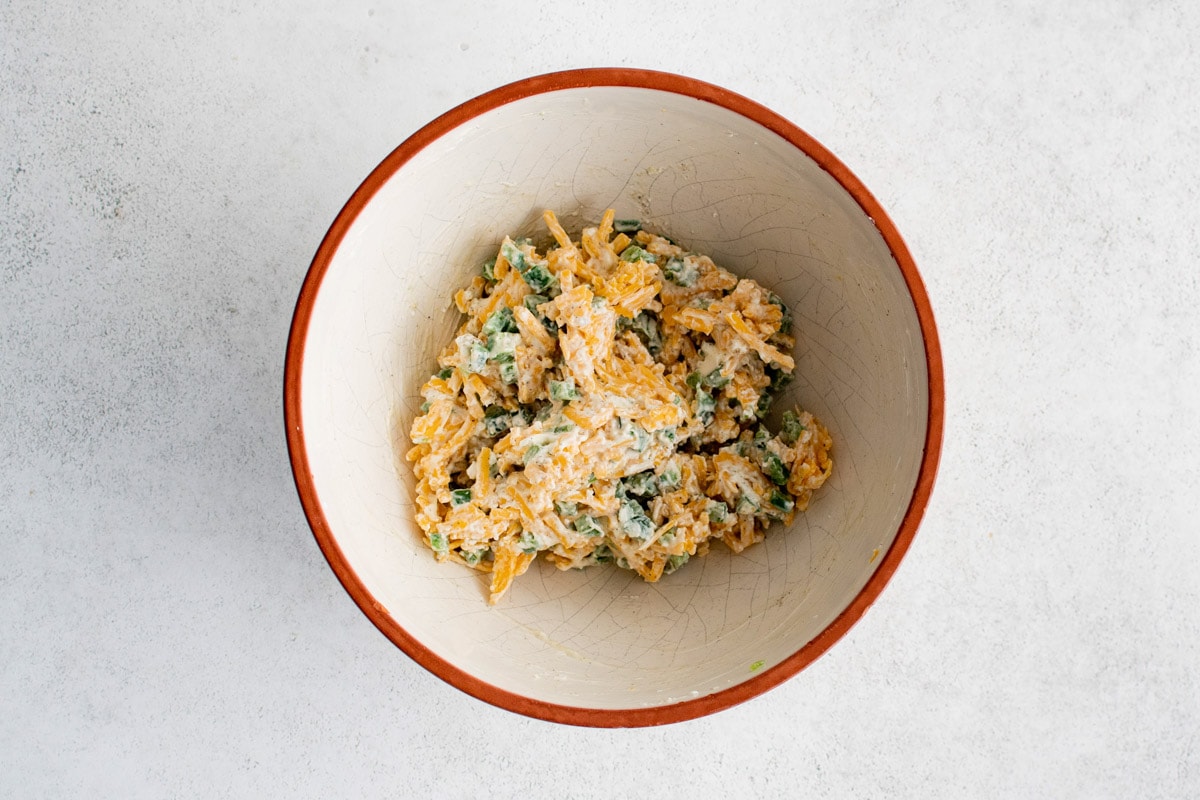 Diced jalapenos, shredded cheddar and cream cheese mixed together in a bowl.