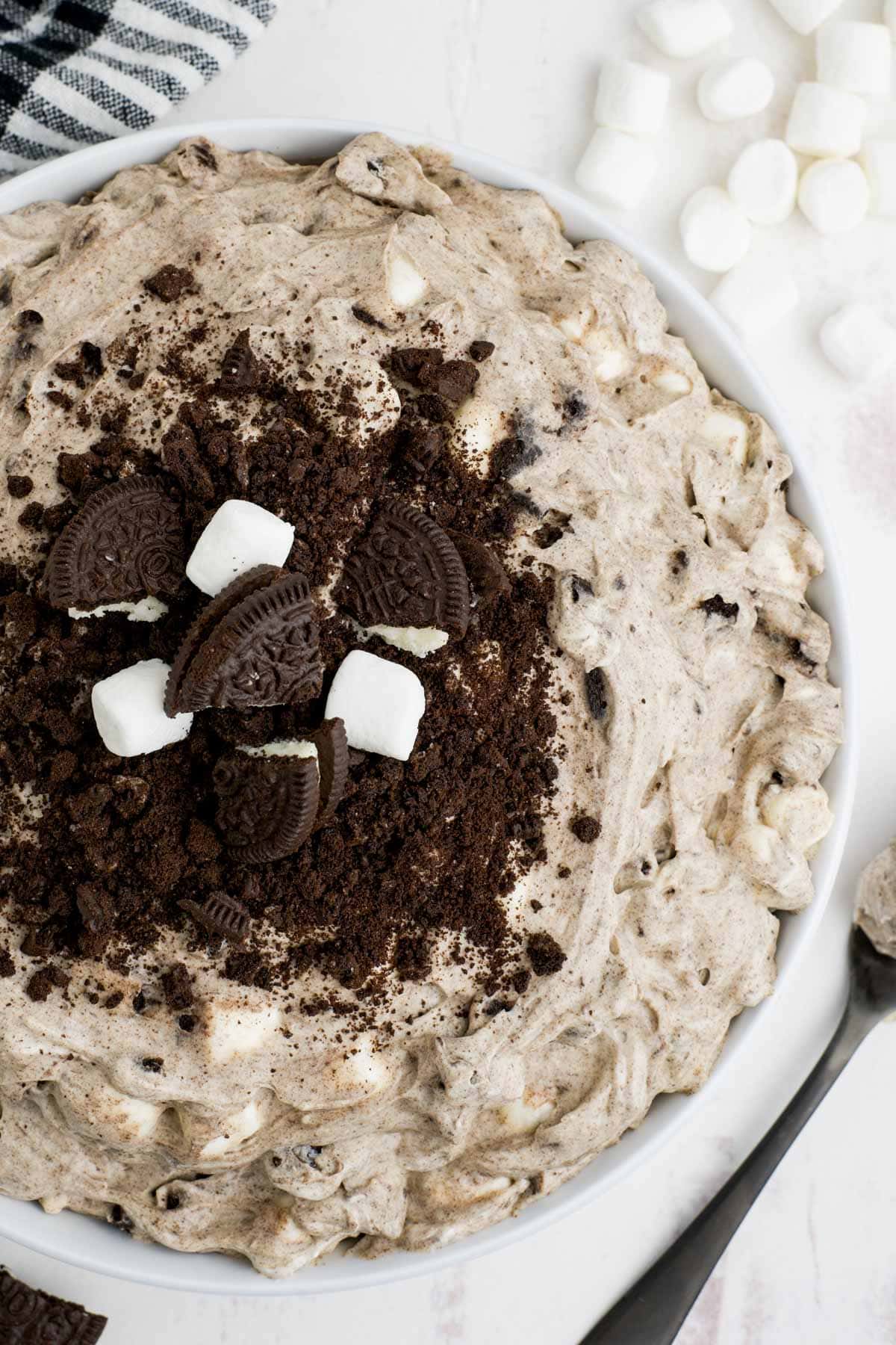 Chocolate Oreo fluff in a large white serving bowl, with crushed oreos and marshmallows on top.