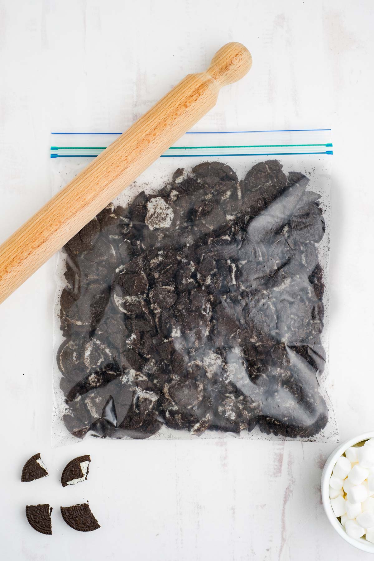 Crushed Oreo cookies in a ziploc bag with a wooden rolling pin.