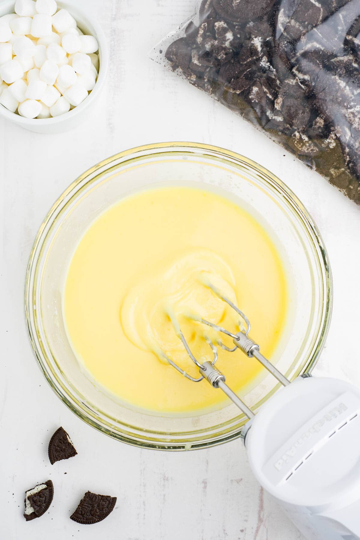 Electric hand mixer in a large bowl, beating vanilla pudding.