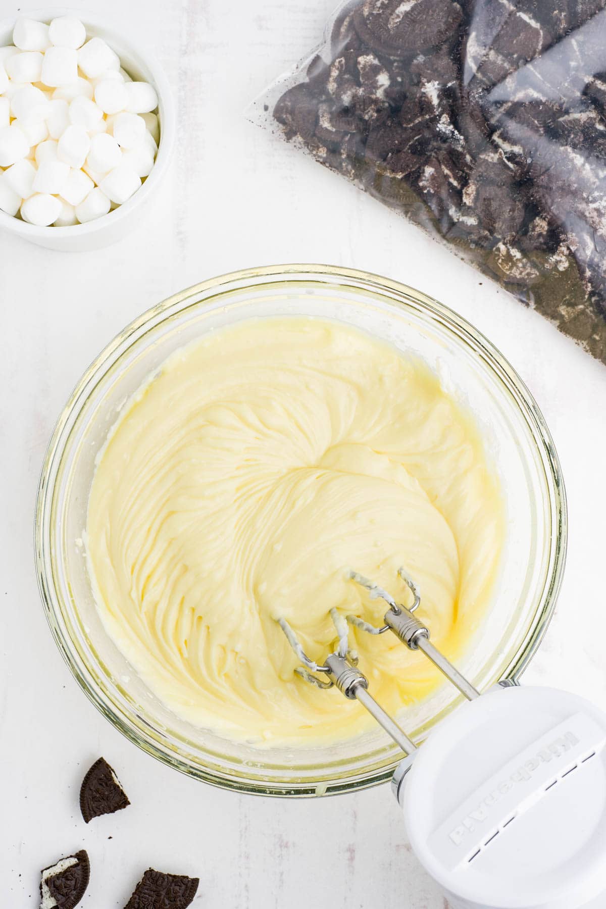 Beating vanilla pudding and cream cheese with a handheld mixer.