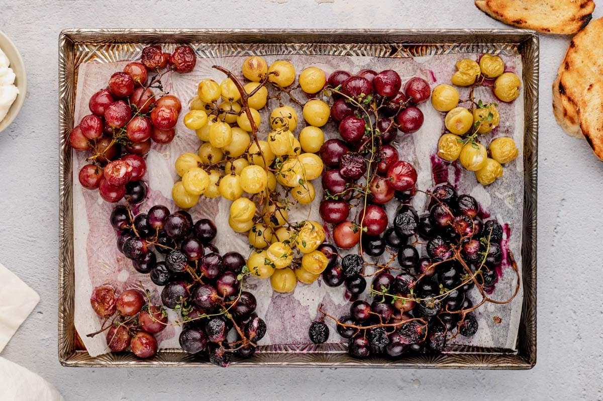 Grapes to be roasted on a parchment paper covered baking sheet.