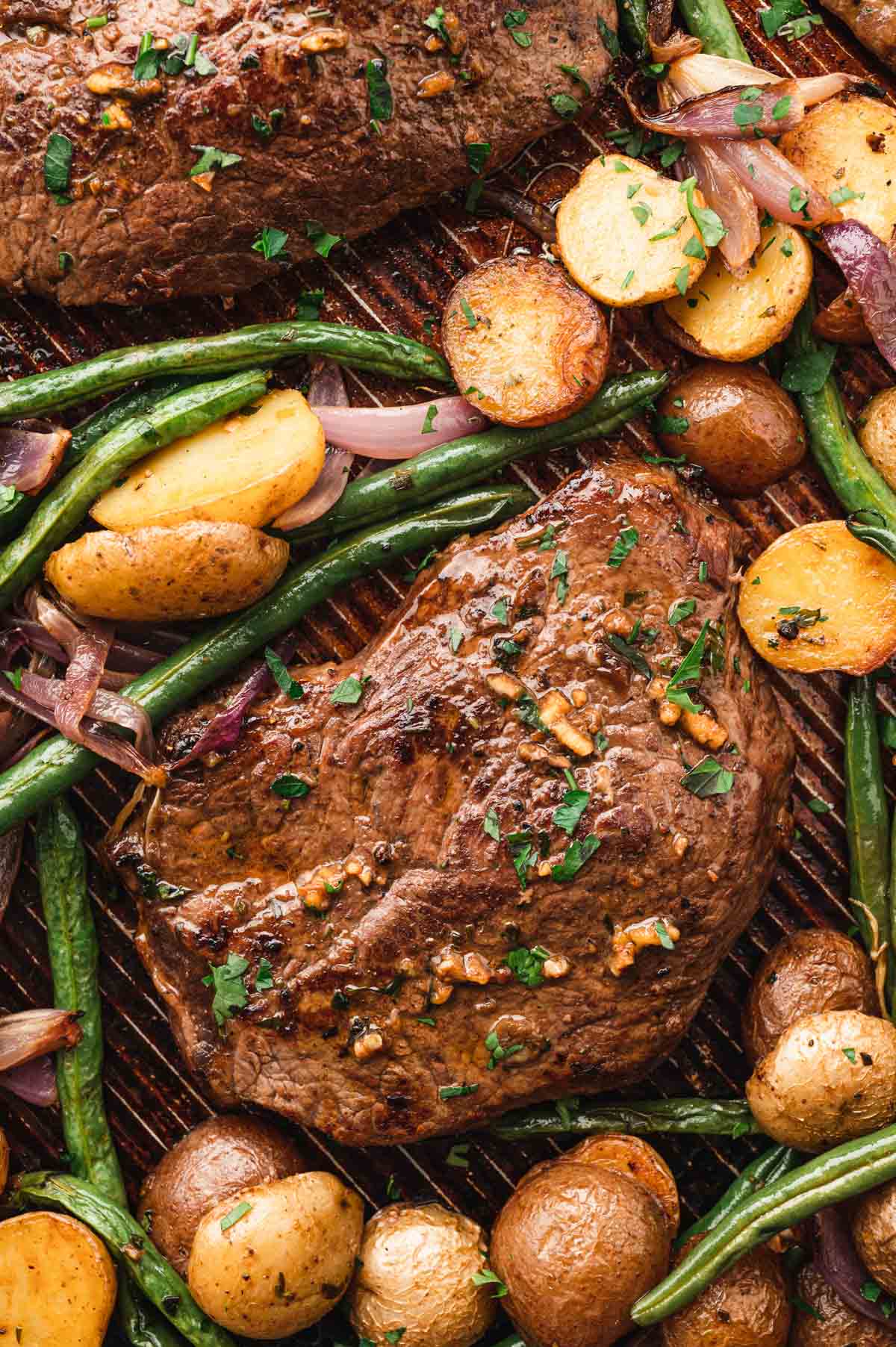 Cooked juicy steak, green beans and potatoes on a sheet pan.