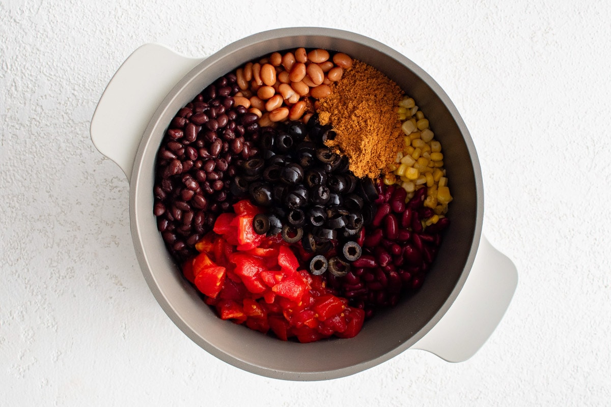 Beans, olives, corn and tomatoes added to a pot.