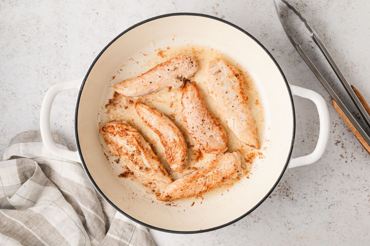 Chicken tenders cooking in a large skillet.