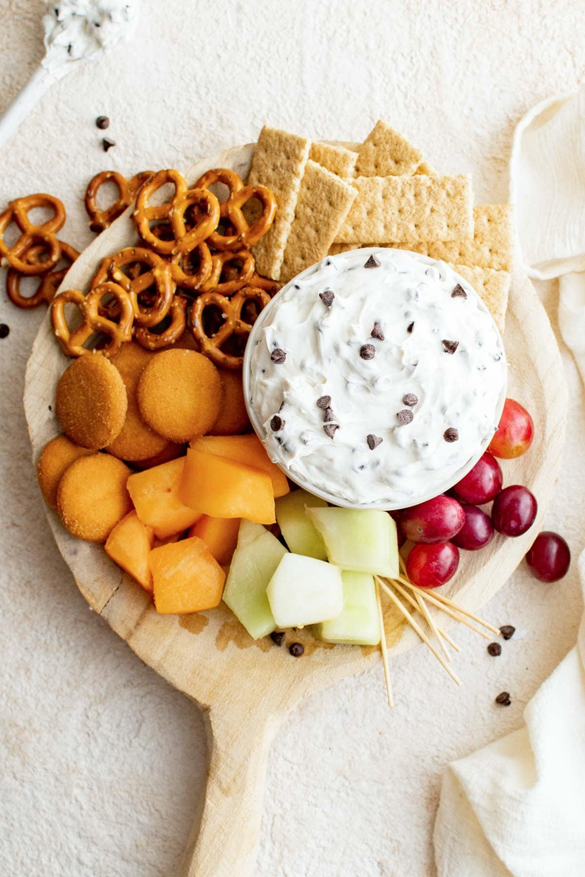 Chocolate chip dip, surrounded on a tray by nilla wafers, pretzels, cantalope and cherries. 