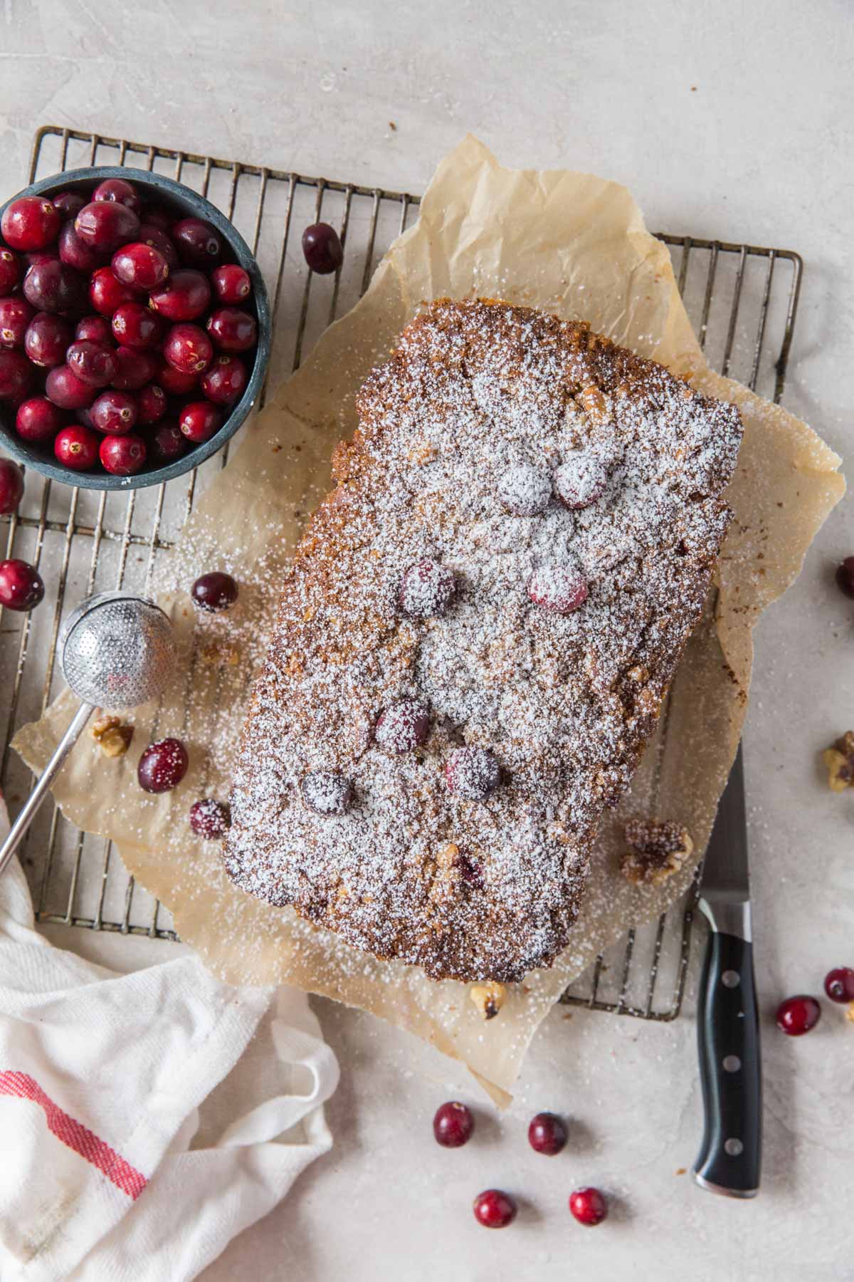 Loaf of cranberry walnut bread on a rack with fresh cranberries.
