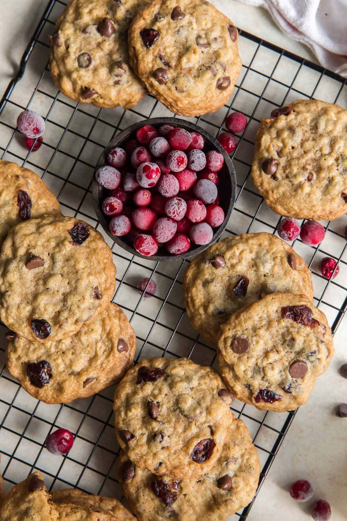 Chocolate chip cranberry cookies on a cooling rack and a small bowl of cranberries.