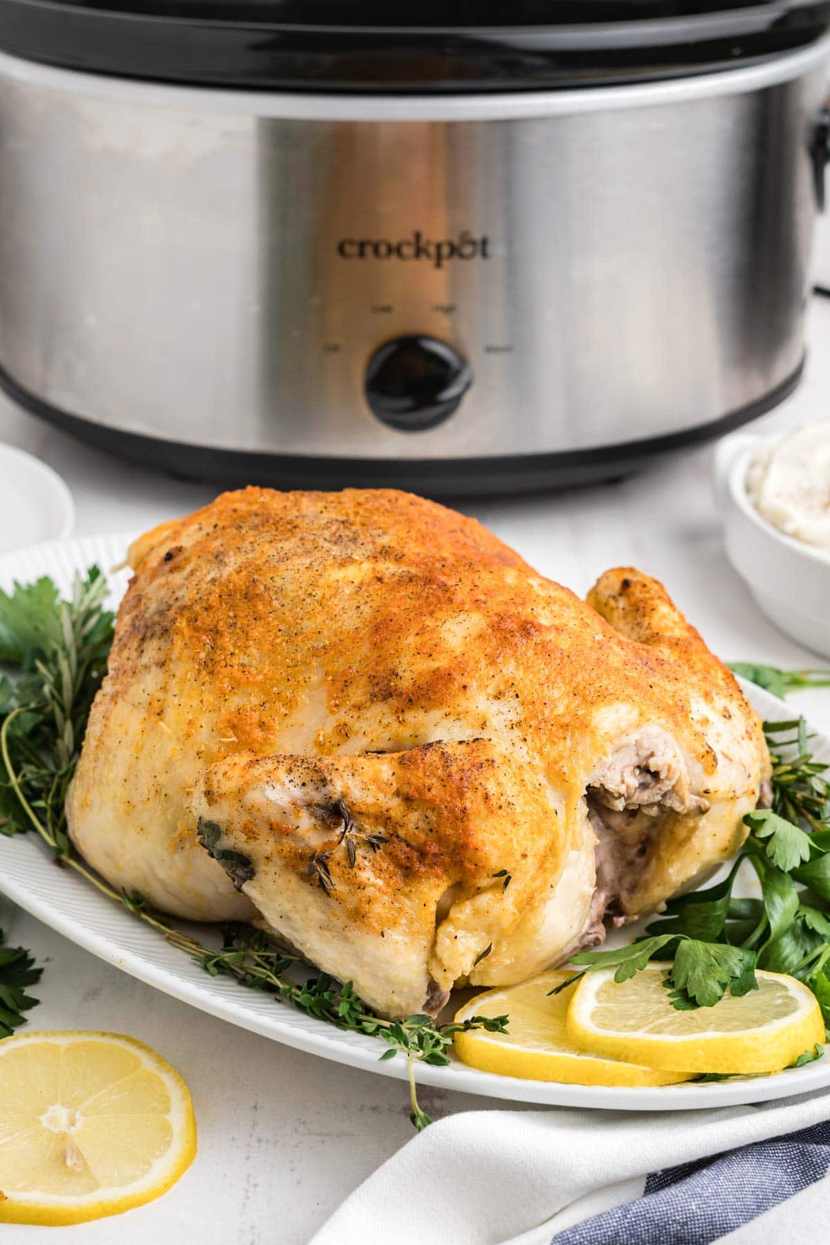 whole chicken on a white platter in front of a slow cooker.