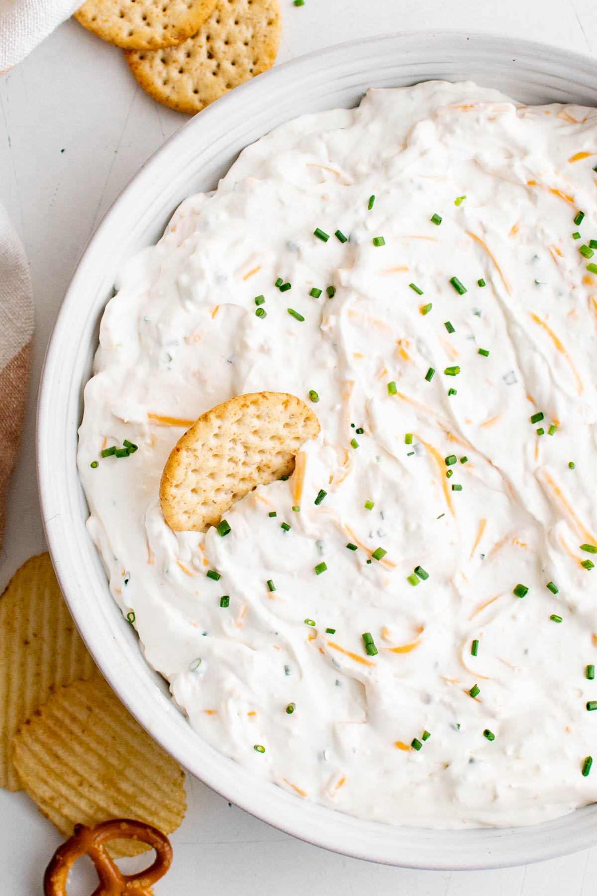 Cream cheese with shredded cheddar in a large bowl with crackers.