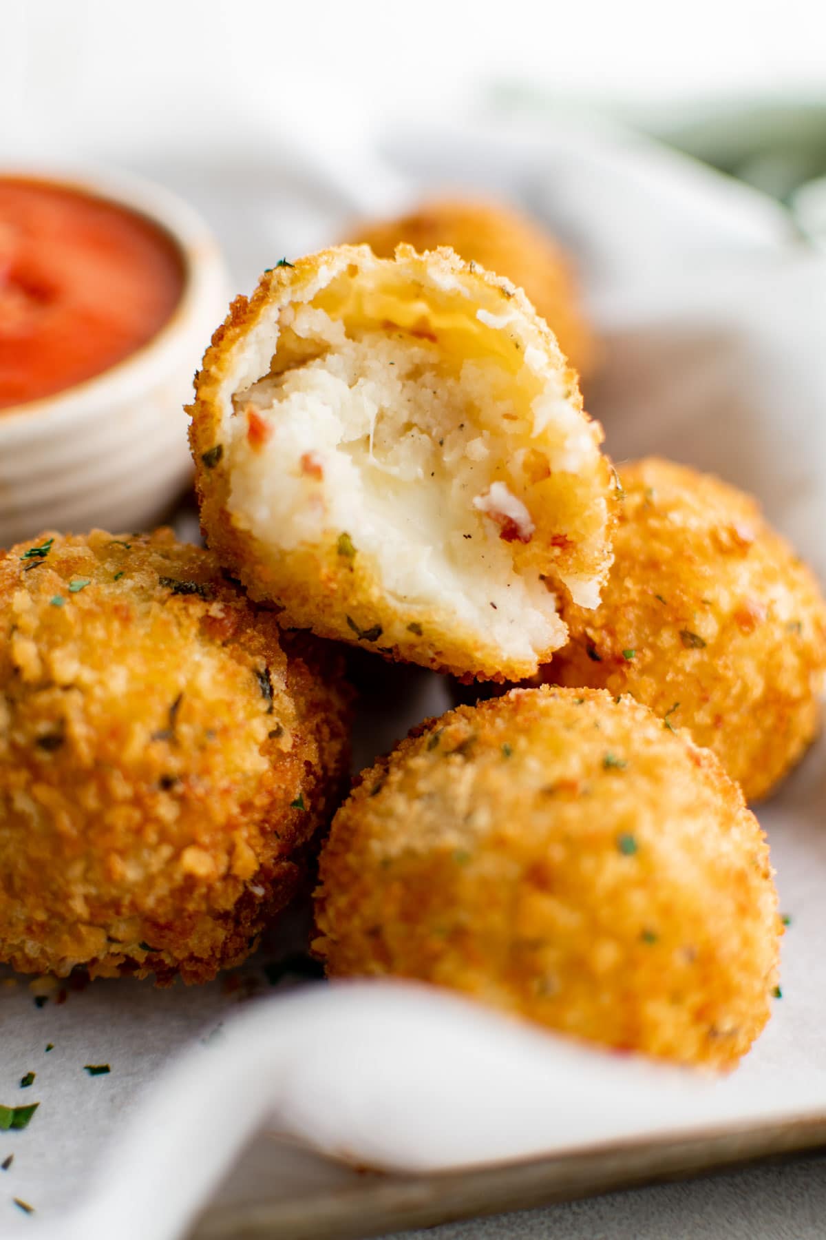 Crispy fried potato cheese balls in a stack, with the top one split open to show cheese oozing out.