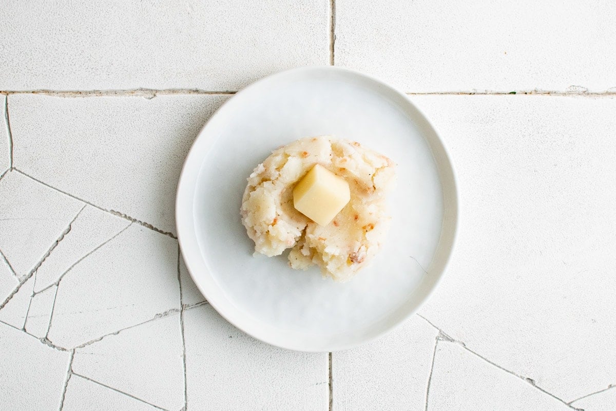 A scoop of mashed potato on a white plate with a cube of cheese in the center.