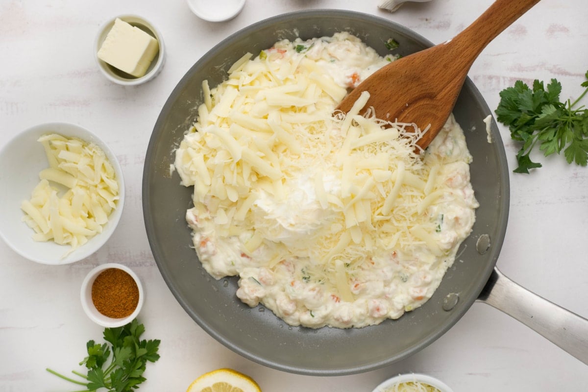 Cream cheese, shrimp and shredded cheese in a skillet with a wooden spatula.