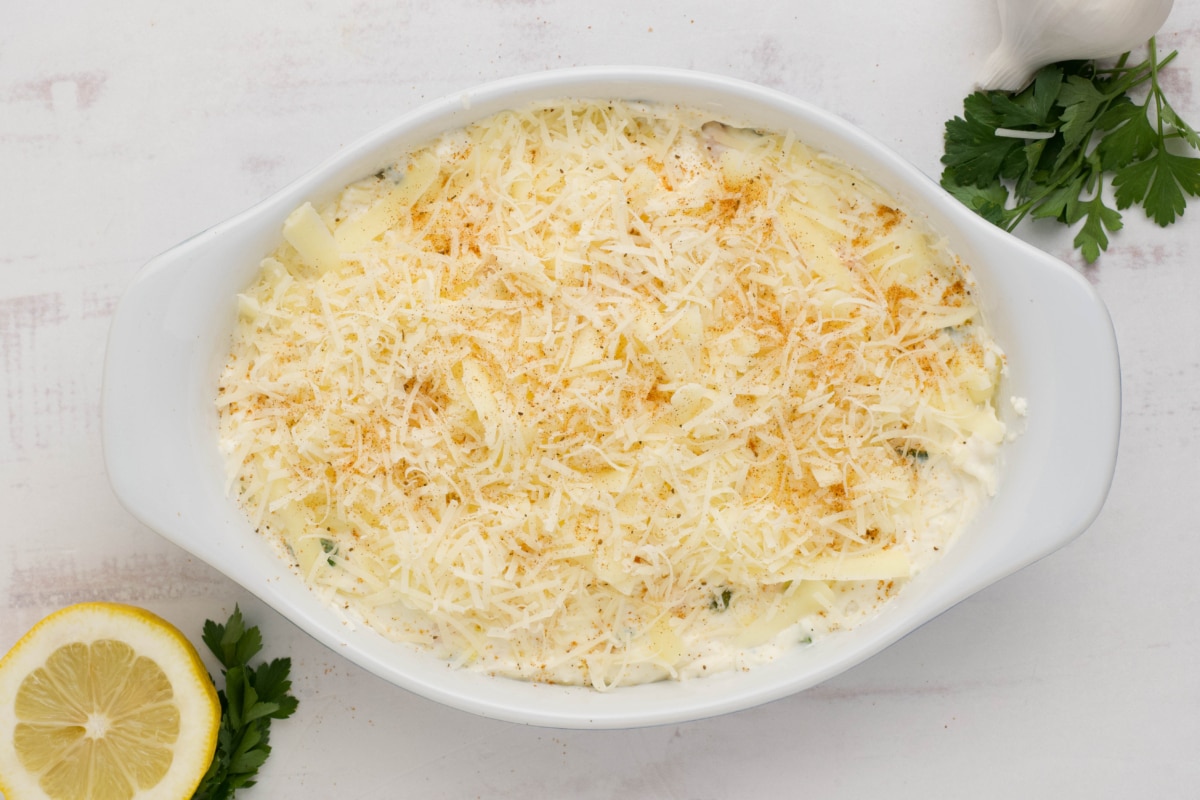 Shrimp and cream cheese dip in a white baking dish with shredded cheese on top.