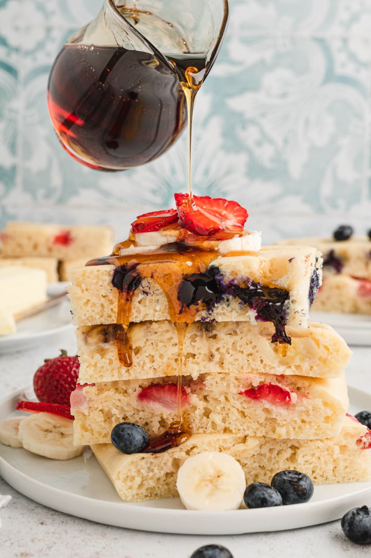 Stack of square pancakes with fruit and syrup.