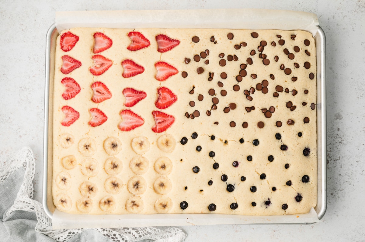 Baked sheet pan pancake with bananas, blueberries, strawberries and chocolate chips.