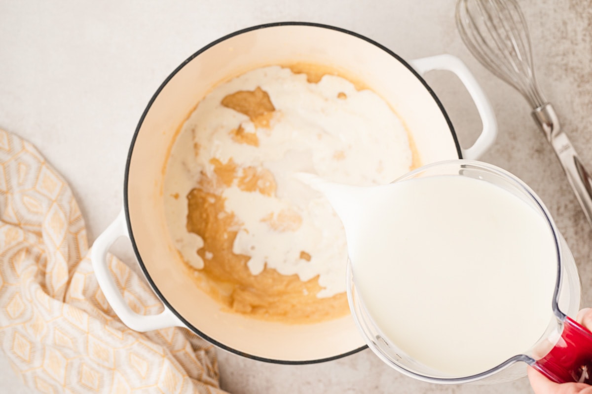 Milk being poured into a pot with a roux.