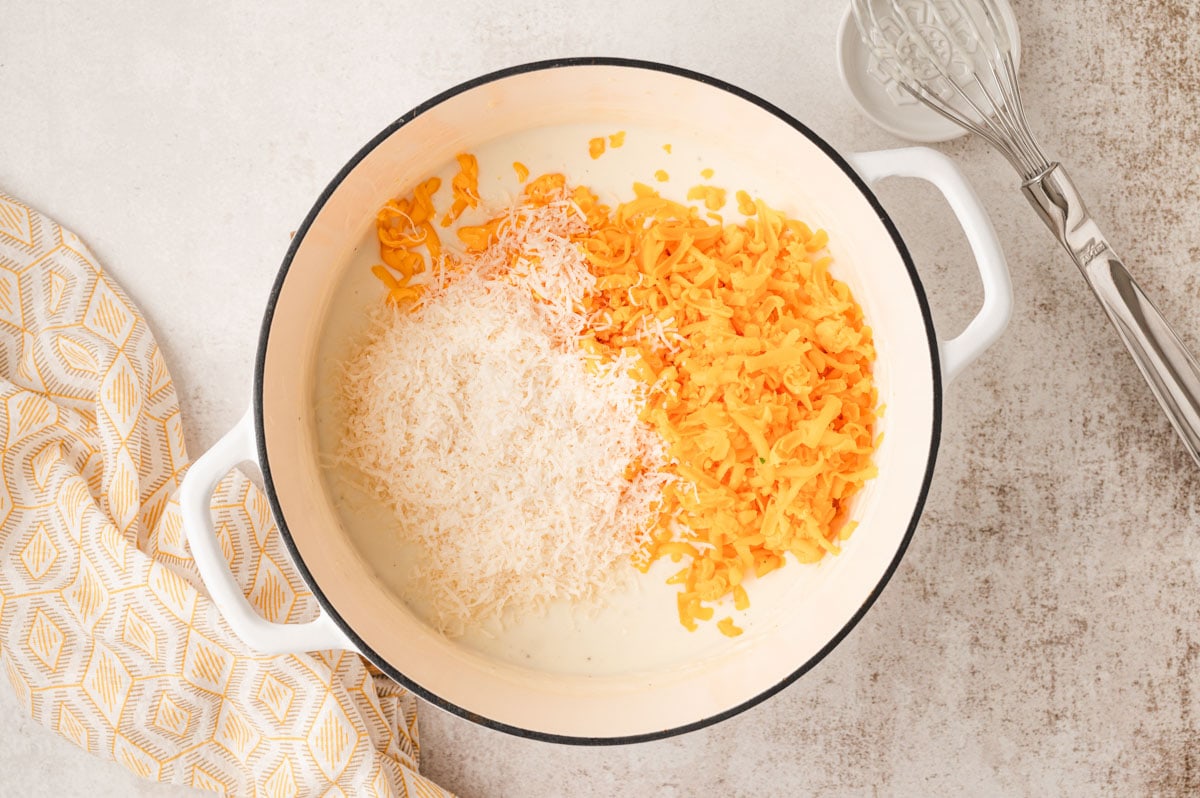 Shredded orange and white cheese in a large pot, sitting on top of a bechamel sauce.