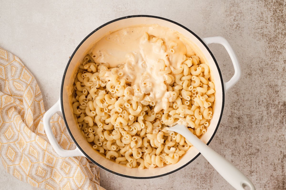 Cooked macaroni and a cheese sauce being stirred together in a large pot and with a wooden spoon.